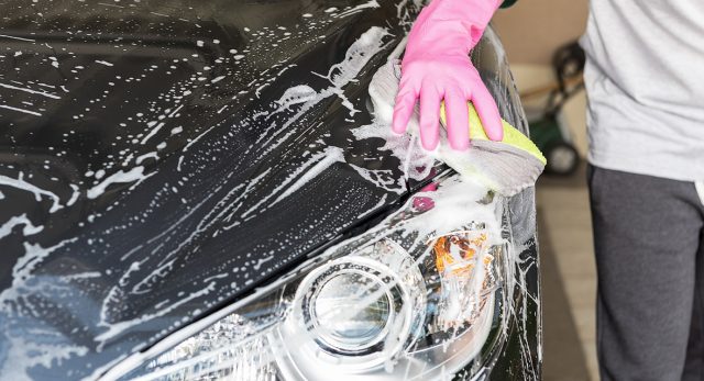 Une personne lave sa voiture de couleur noire avec une éponge et du savon