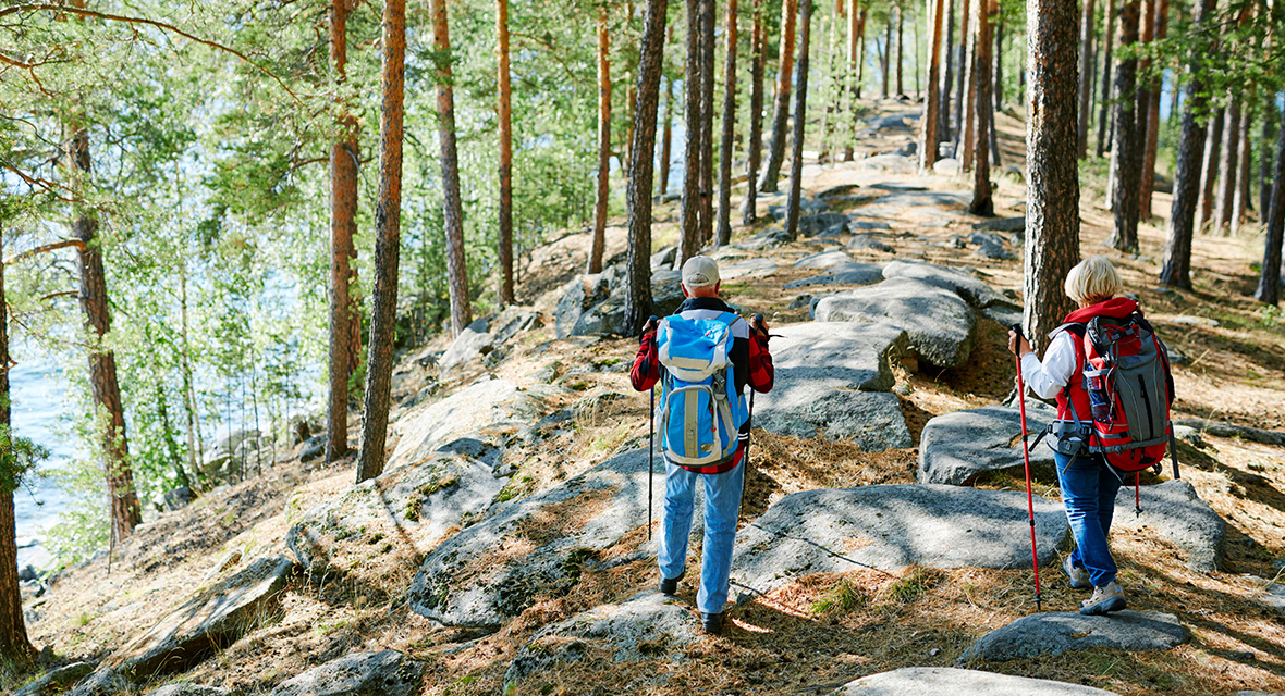 Un homme et une femme qui marchent en forêt avec des bâtons de randonnée et un sac à dos